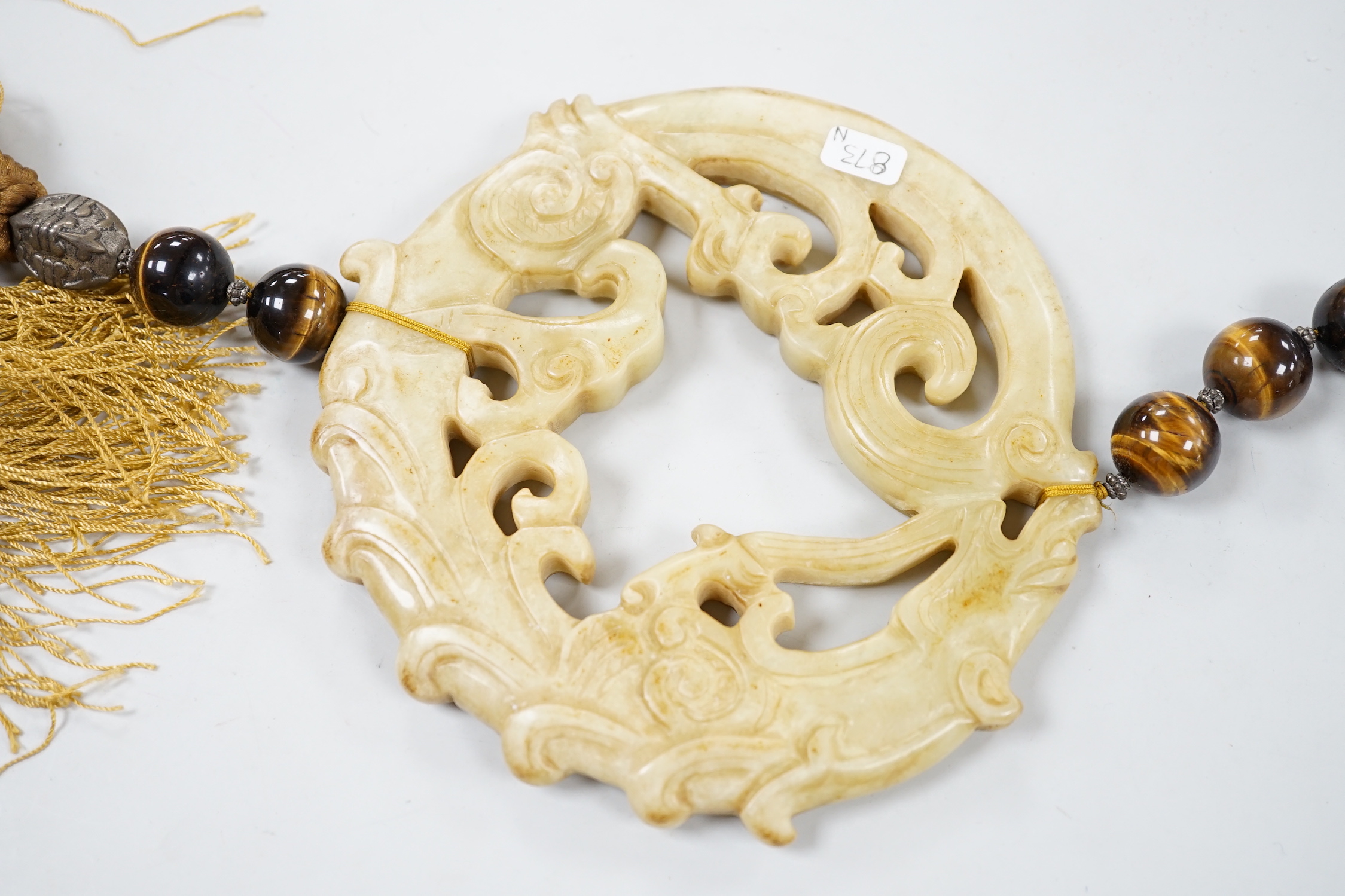 A large Chinese bowenite jade disc, threaded with tiger's eye beads and long silk tassel, 90cm long